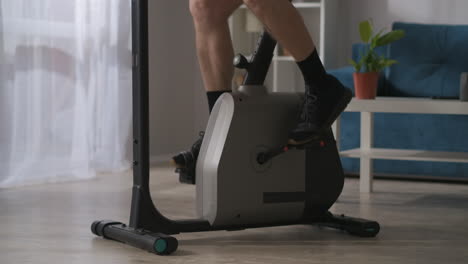 sport-at-home-during-self-isolation-male-legs-are-spinning-pedals-of-stationary-bicycle-in-living-room-closeup-view-training-at-home-healthy-lifestyle